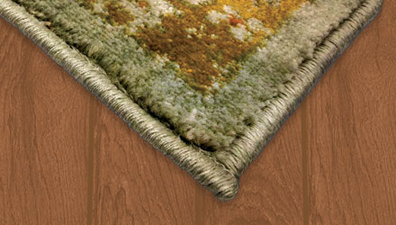 A low pile area rug with a green and gold motif resting upon a hardwood floor