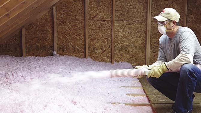 Man applying pink spray foam insulation in an attic