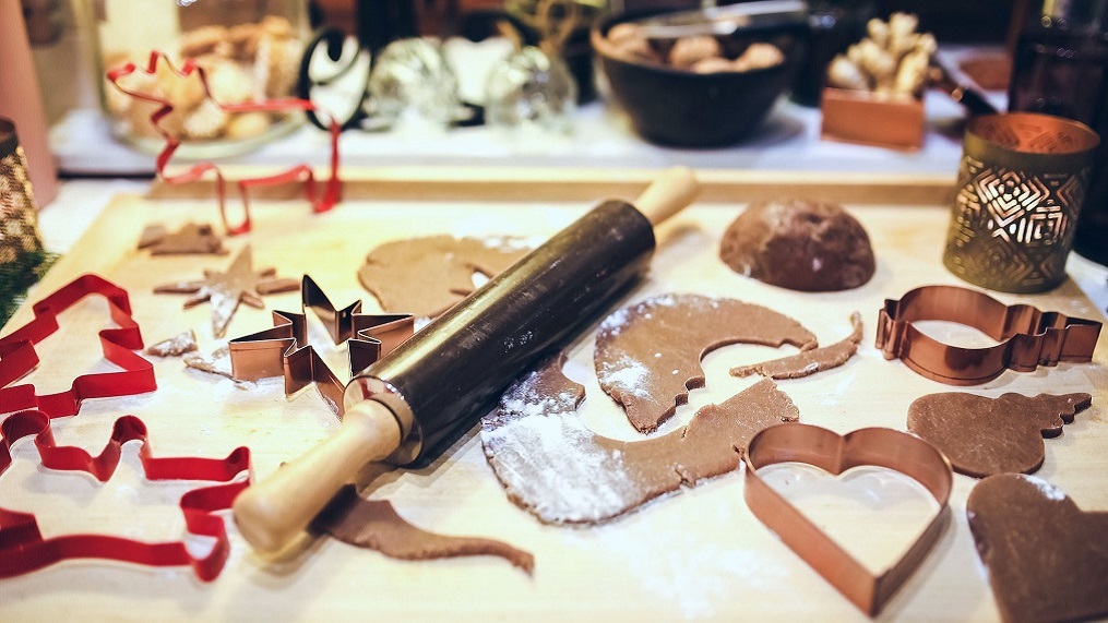 Pastry board with cookie dough, rolling pin and cookie cutters.  
