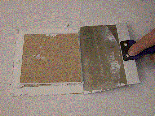Person putting joint compound on the paper part of the back of a drywall patch